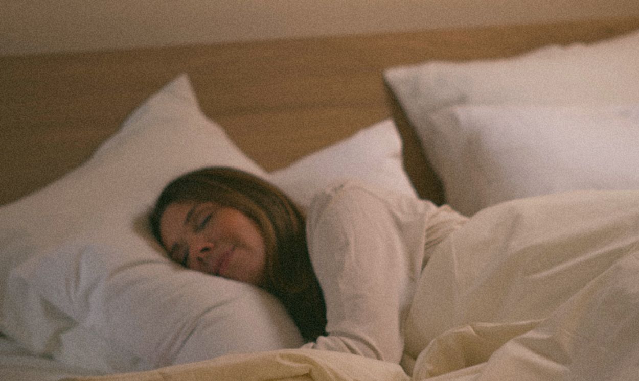 Donna che dorme serenamente in un letto Kipli con cuscini e biancheria da letto in materiali naturali.