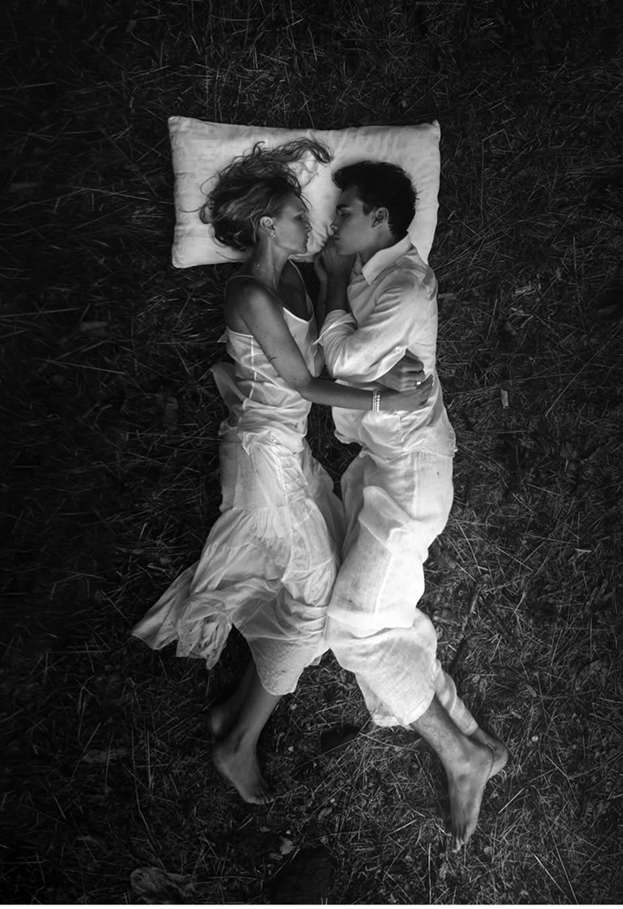 Due persone distese una accanto all’altra sull’erba, appoggiate a un cuscino, che illustrano un momento di relax, di intimità e di sonno naturale all’aria aperta.