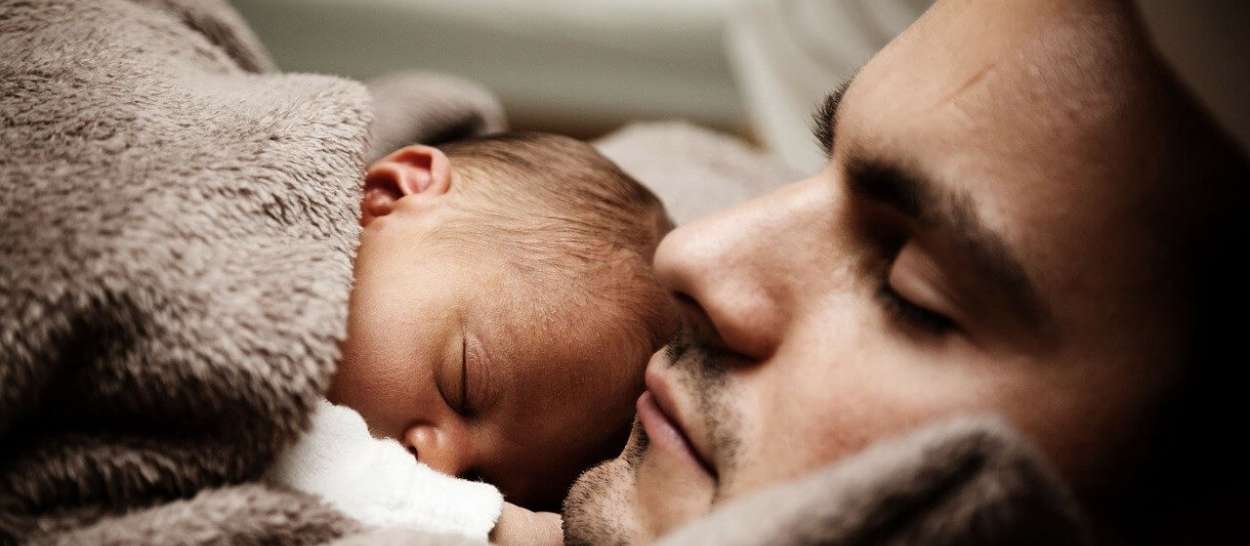 Papa, der neben dem Neugeborenen schläft, beide in eine weiche Decke gehüllt