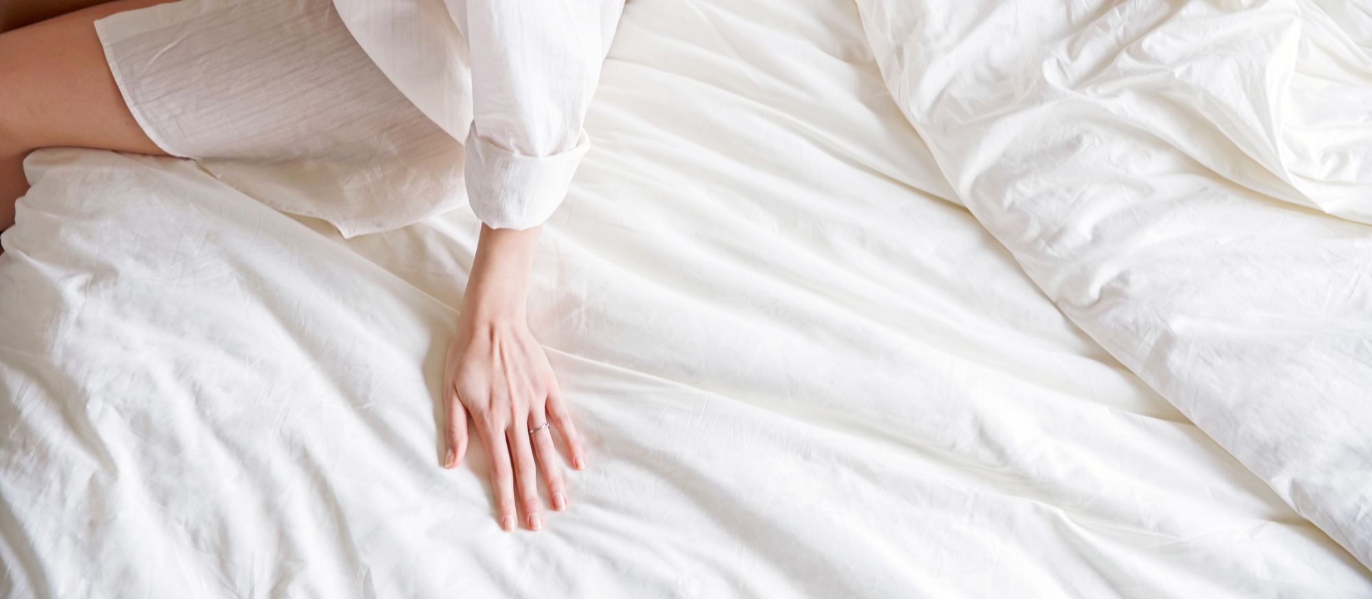 Mano appoggiata su un lenzuolo in cotone biologico bianco, a illustrare la morbidezza e la qualità del completo da letto Kipli.