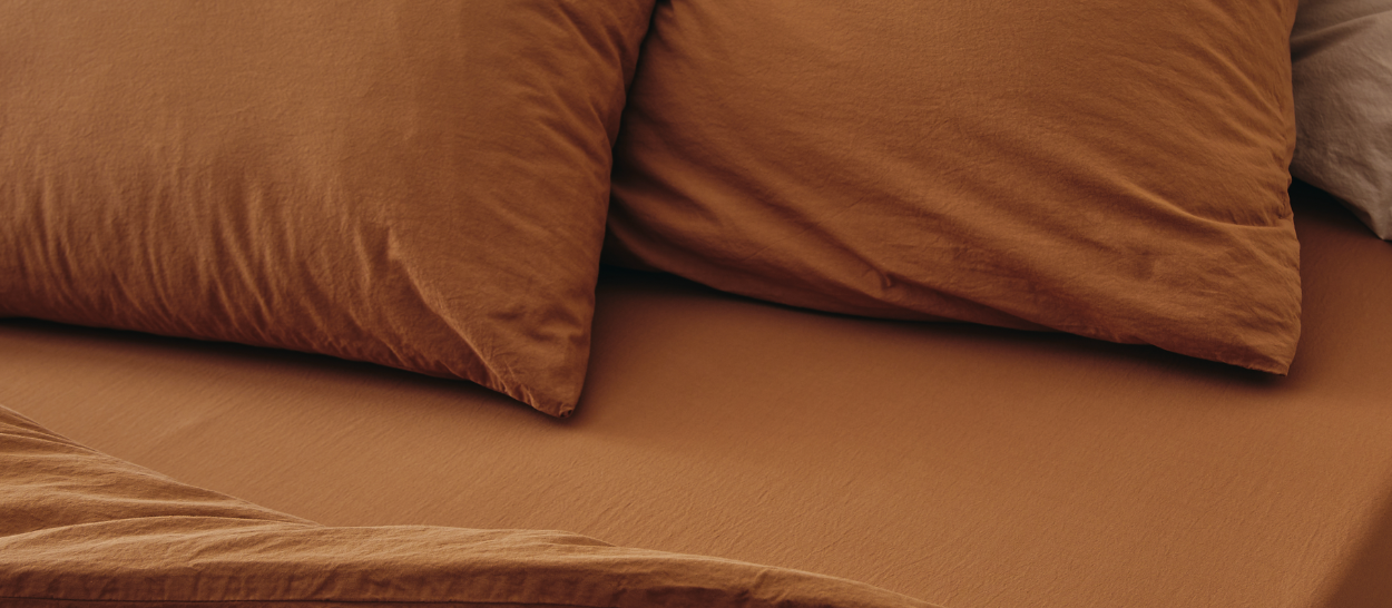 Biancheria da letto in cotone biologico color terracotta su un letto Kipli, a illustrare un ambiente accogliente e tessuti naturali per una camera da letto salubre.