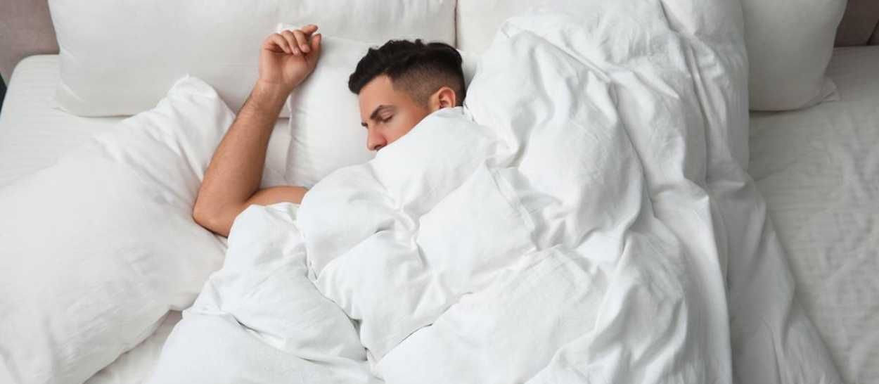 Un uomo che dorme profondamente in un letto accogliente, a simboleggiare la necessità di dormire più a lungo in inverno.