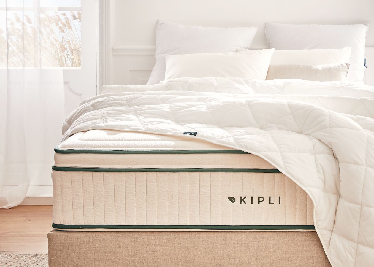 Materasso Kipli in lattice naturale con piumone e cuscini bianchi, a illustrare una biancheria da letto sana e sostenibile in una camera luminosa.