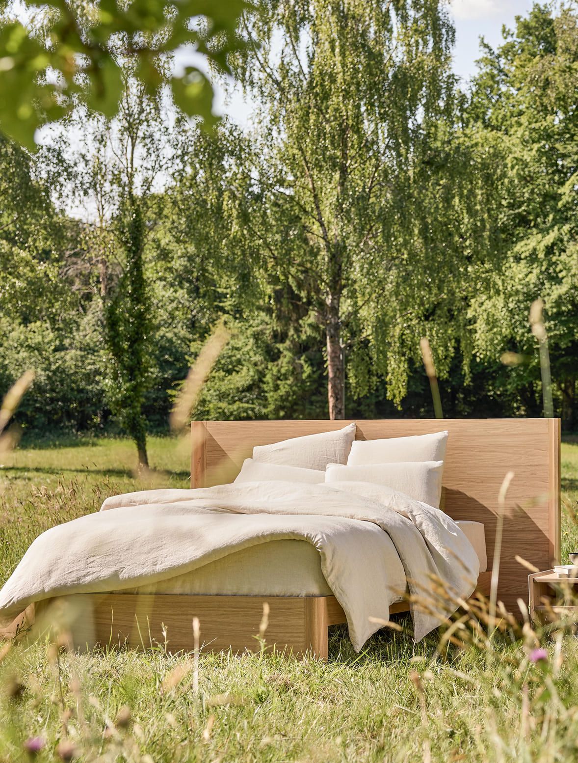 Cama em madeira maciça da Kipli, instalada em plena natureza, com roupa de cama em materiais naturais, ilustrando um quarto ecológico e um sono saudável.