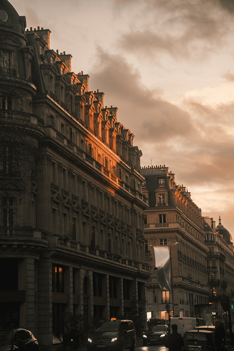 Facciate in stile Haussmann a Parigi al tramonto, con la luce dorata sui tetti e il viavai di persone ai piedi dei palazzi.