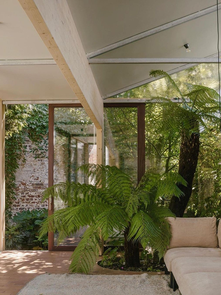 Luminoso salotto arredato in stile naturale, con grandi piante verdi e una vetrata che si affaccia su un giardino, a creare un ambiente rilassante ed eco-responsabile.