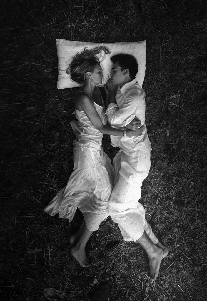 Due persone distese una accanto all’altra sull’erba, appoggiate a un cuscino, che illustrano un momento di relax, di intimità e di sonno naturale all’aria aperta.