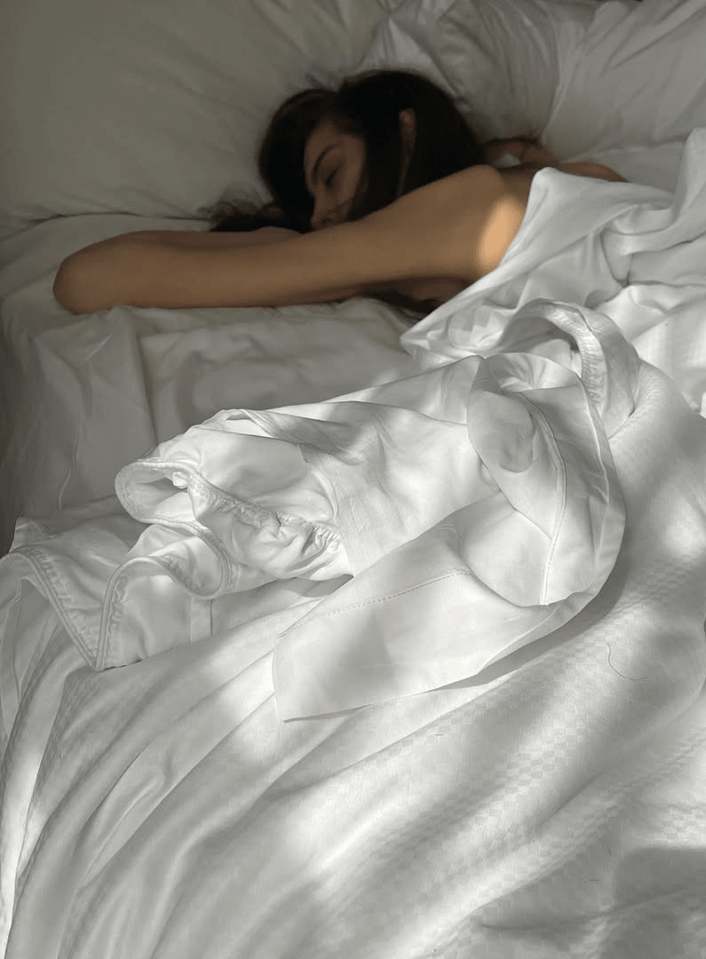 Una persona addormentata tra lenzuola bianche inondate di luce naturale, a simboleggiare un sonno ristoratore e una biancheria da letto confortevole e rilassante.
