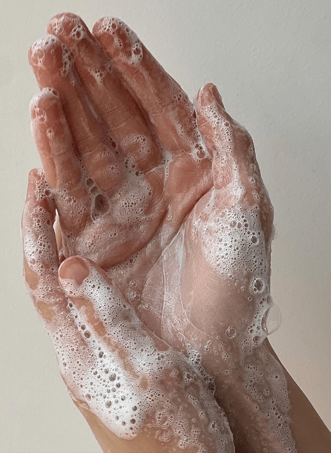 Mani insaponate e ricoperte di schiuma, che illustrano un gesto di pulizia delicato e naturale per prendersi cura della propria biancheria da letto e garantire un ambiente sano in cui dormire.