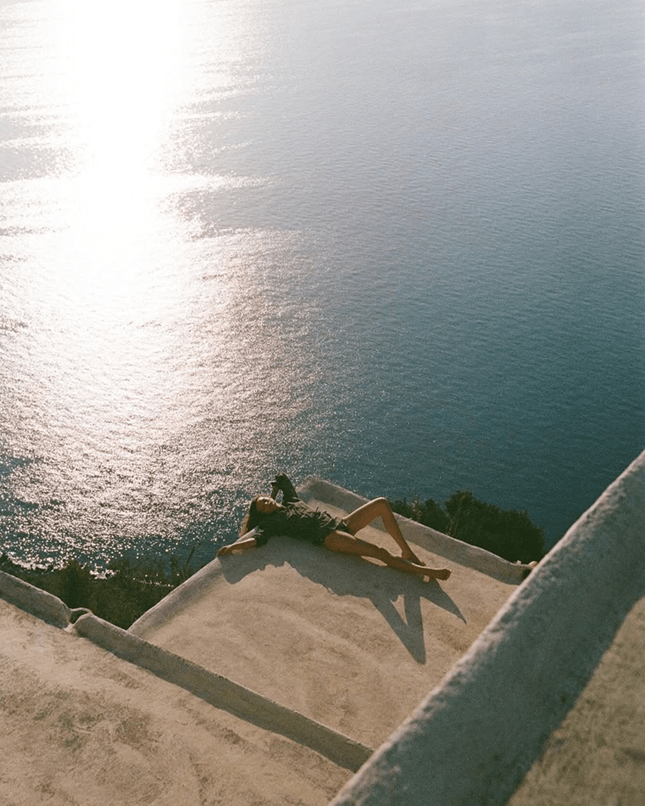 Mulher deitada ao sol, de frente para o mar, representando um momento de descontração e bem-estar em plena natureza, símbolo de um estilo de vida sereno e revigorante.
