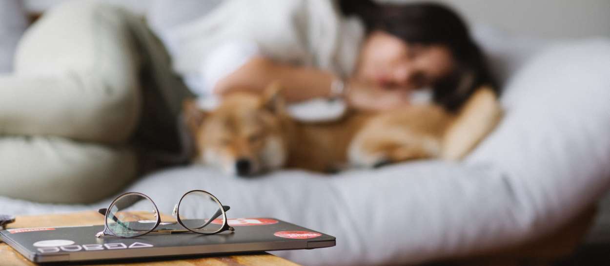 En kvinde, der hviler sig på sengen med sin hund, mens hendes briller ligger på bordet